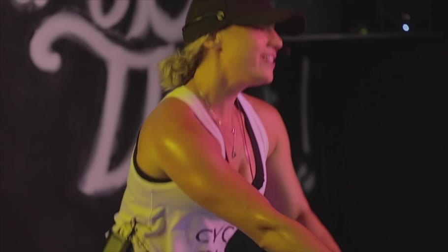 A CbK coach on the bike, raising her arm toward the class in pink light